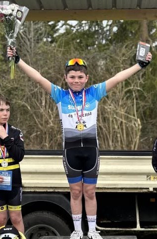 Un jeune coureur de l’école de cyclisme sur le podium, médaille autour du cou et bouquet à la main
